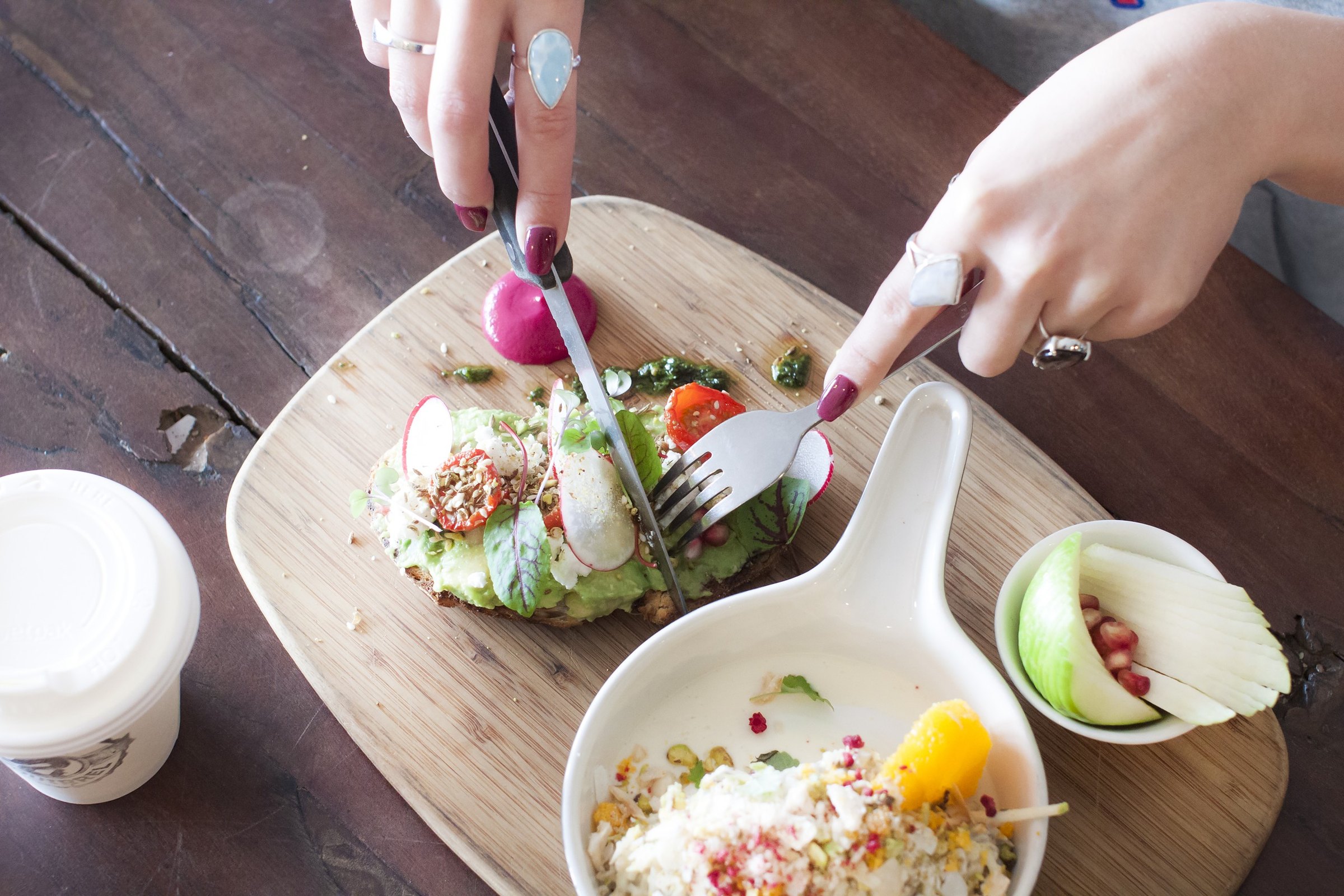 Avocado toast being cut, with a grain salad and coffee