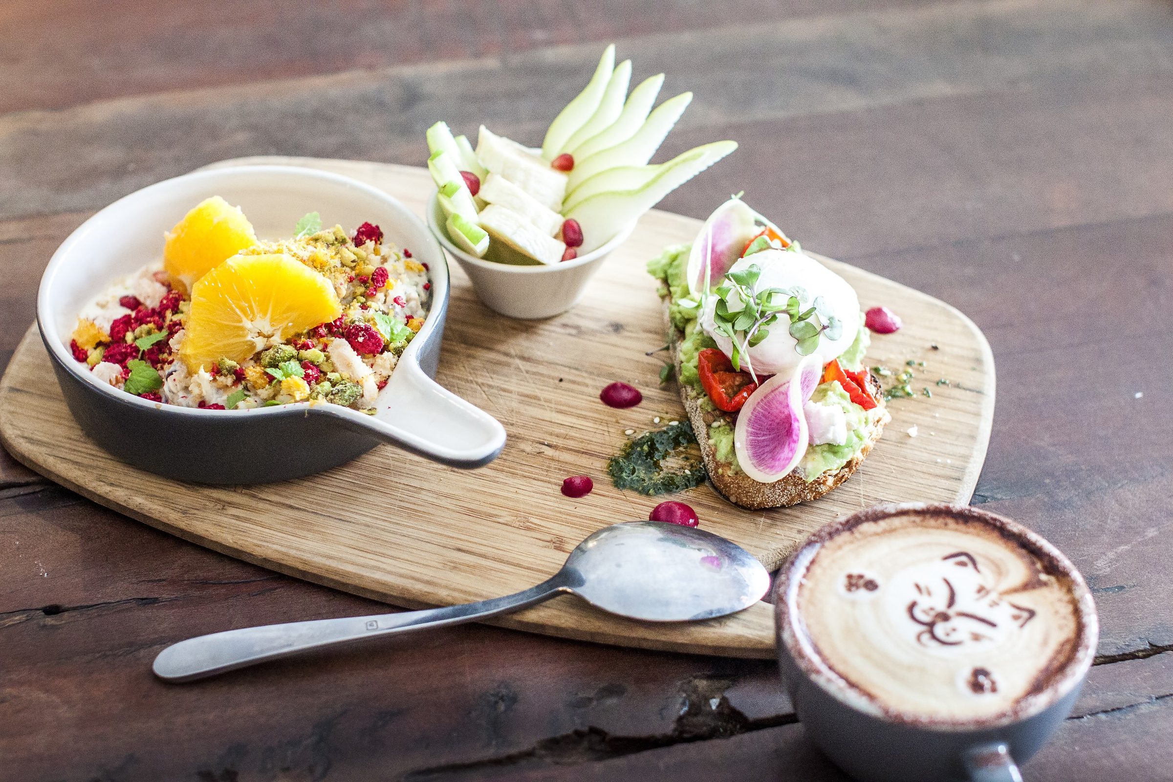 A grain bowl, smashed avocado toast and a latte on a timber board at Black Squirrel