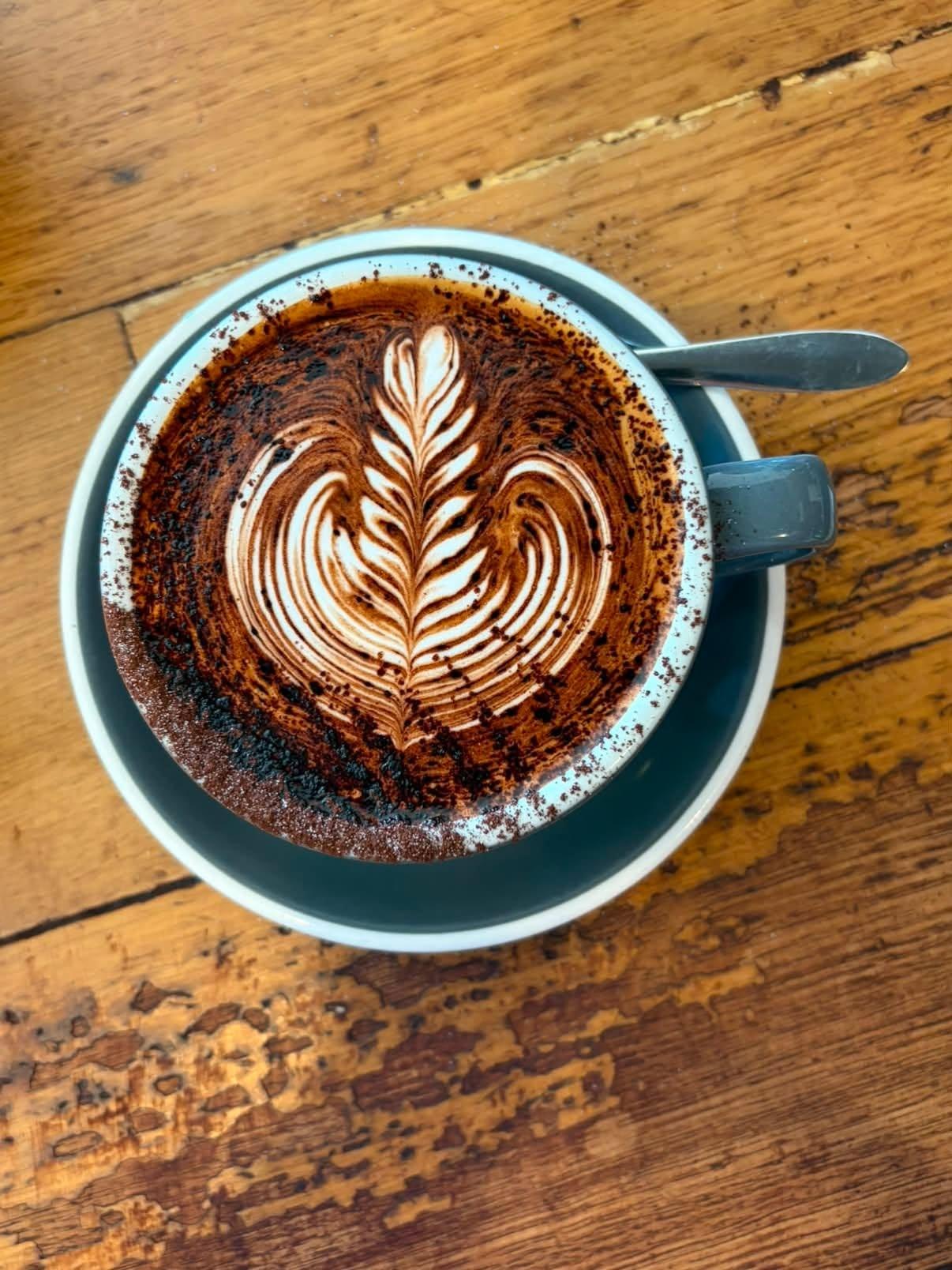 A latte with rosetta latte art on a timber table