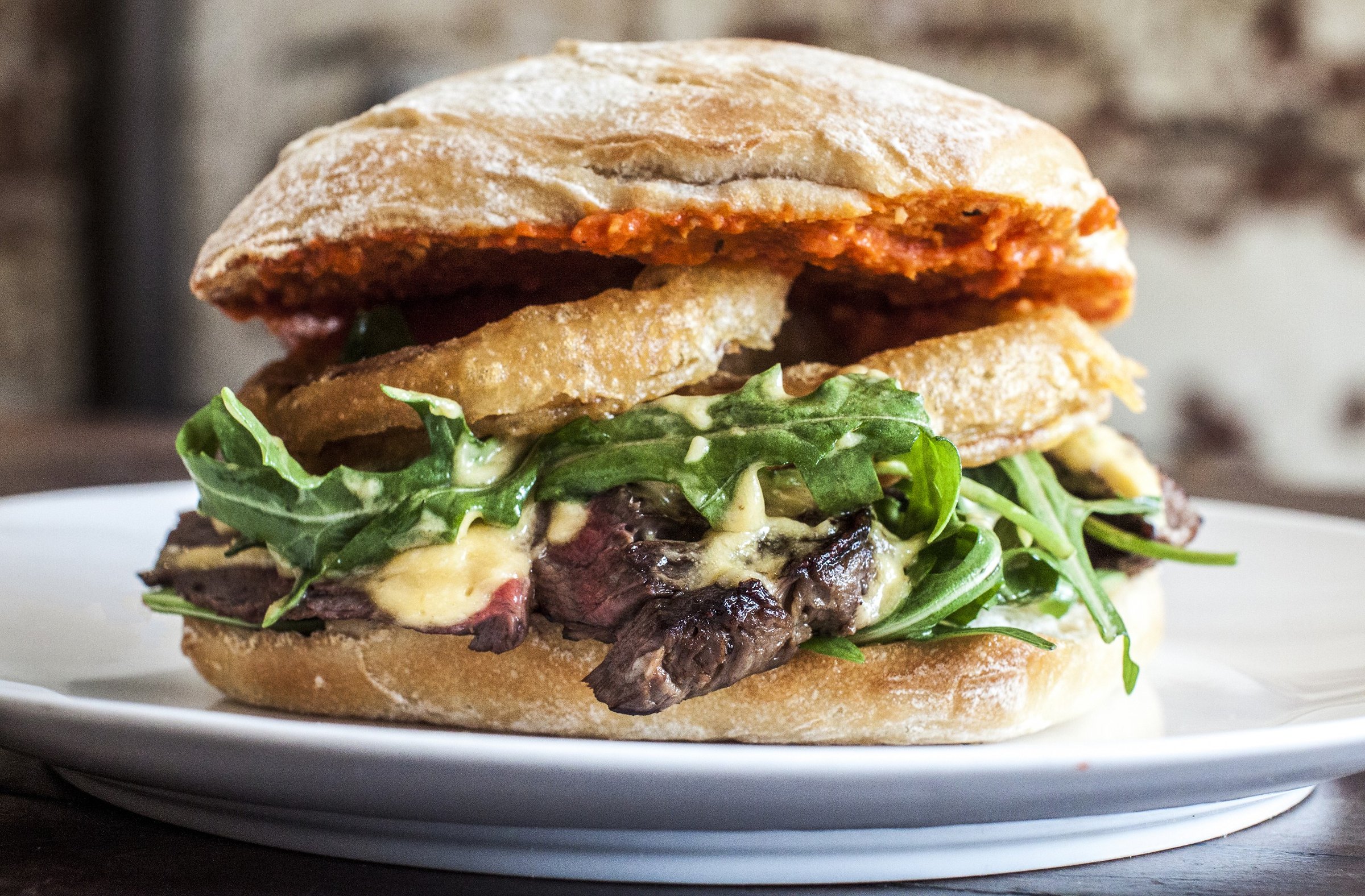 Steak sandwich with onion rings and rocket in a toasted roll